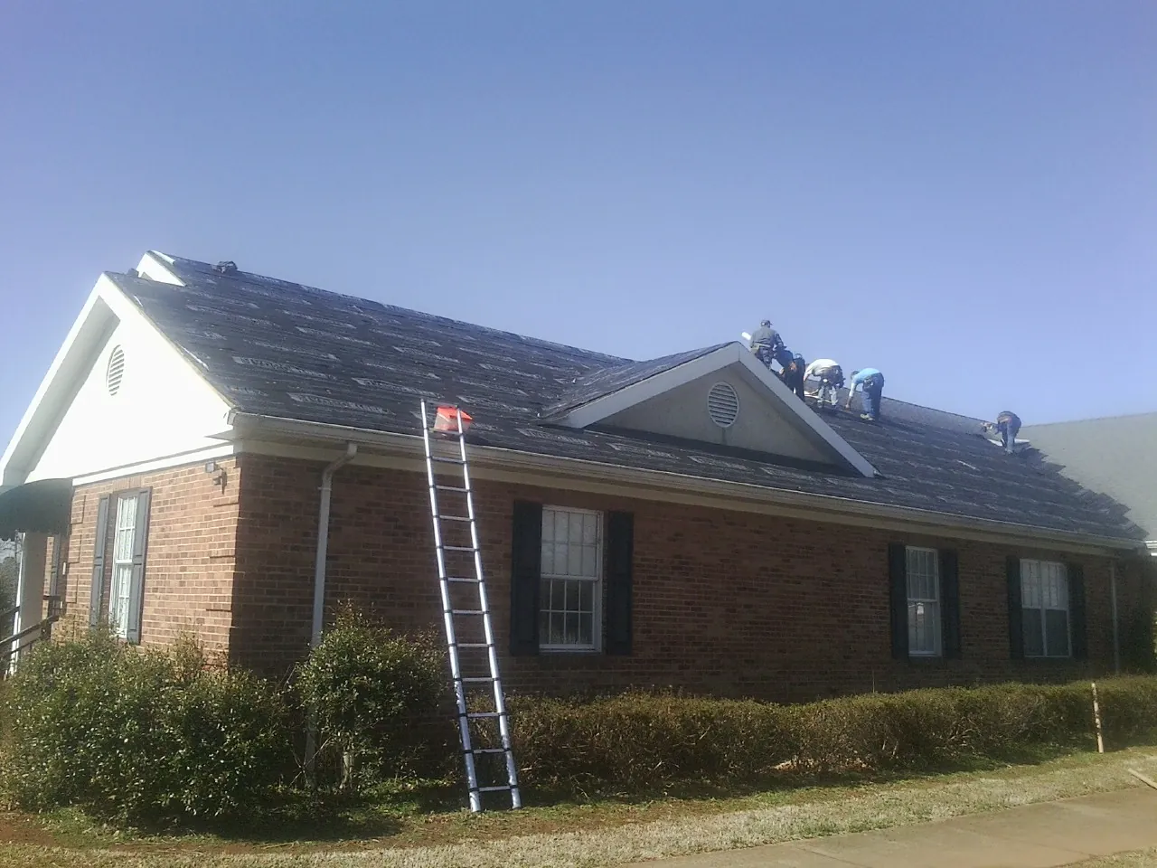 Crew tearing shingles off a brick ranch roof with a ladder set — Emergency Roof Repair work by our crew in Fredericksburg