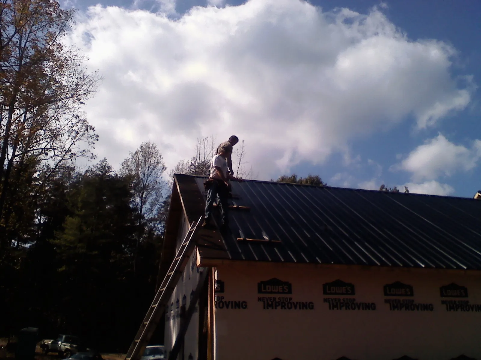 Roofer fastening dark metal panels high against a cloudy sky, from a Roof Inspection job in Fredericksburg